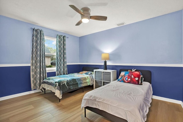 bedroom with a ceiling fan, visible vents, baseboards, and wood finished floors