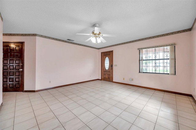 empty room with a textured ceiling, a ceiling fan, visible vents, and baseboards