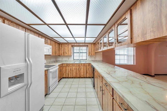 kitchen featuring light tile patterned floors, white appliances, a sink, brown cabinets, and light stone countertops