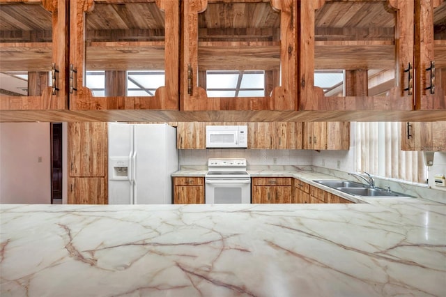 kitchen with brown cabinets, light countertops, decorative backsplash, a sink, and white appliances