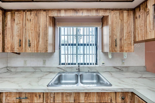 kitchen with brown cabinets, a healthy amount of sunlight, backsplash, and a sink