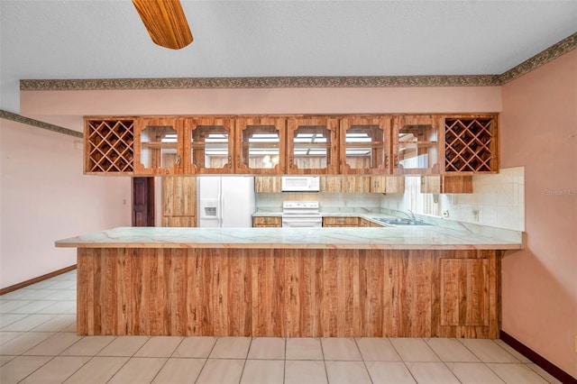 kitchen with a peninsula, white appliances, a sink, baseboards, and light countertops