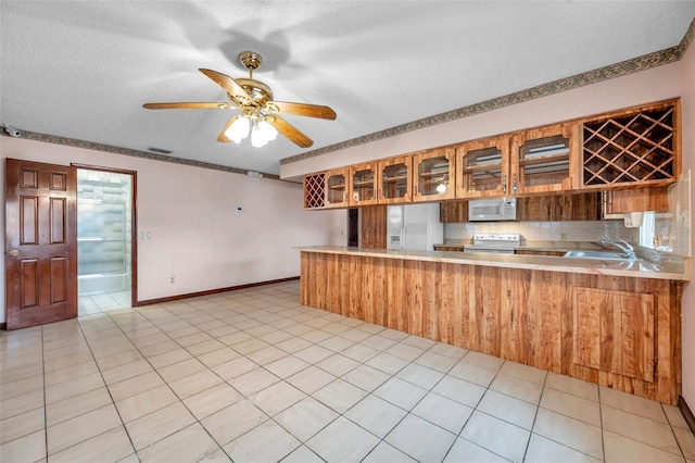 kitchen featuring white appliances, light tile patterned floors, glass insert cabinets, a peninsula, and light countertops