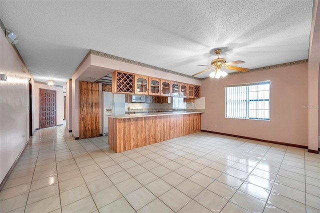 kitchen with light tile patterned floors, a peninsula, white appliances, light countertops, and glass insert cabinets