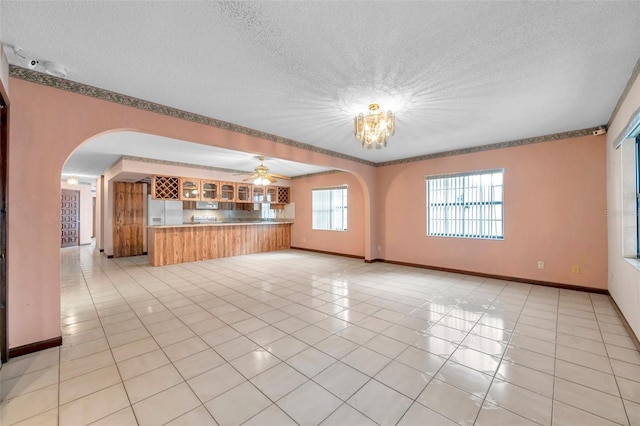 unfurnished living room with arched walkways, a notable chandelier, light tile patterned floors, a textured ceiling, and baseboards