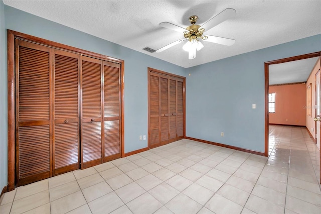 unfurnished bedroom with a textured ceiling, light tile patterned flooring, visible vents, baseboards, and two closets