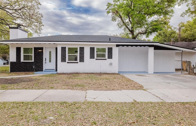 ranch-style home with a shingled roof, concrete driveway, a chimney, and stucco siding