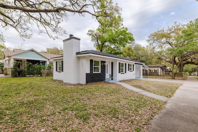 view of front of house featuring a chimney, fence, a front lawn, and stucco siding