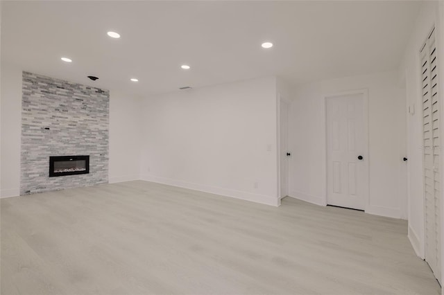 unfurnished living room featuring baseboards, light wood finished floors, a fireplace, and recessed lighting