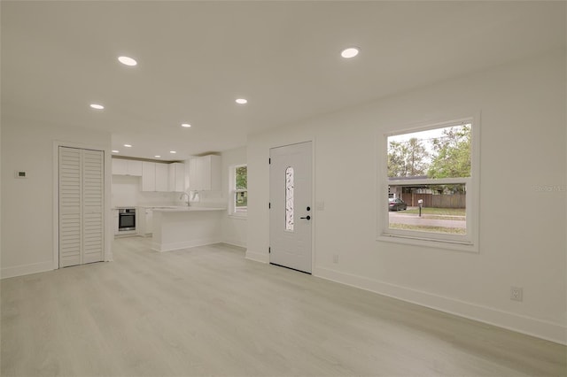 unfurnished living room featuring light wood finished floors, recessed lighting, a sink, and baseboards