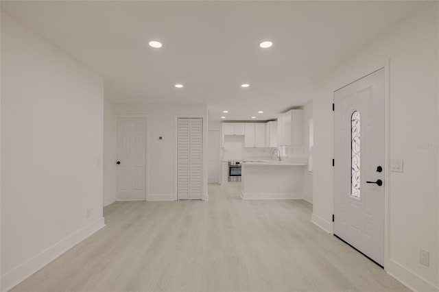 unfurnished living room featuring baseboards, light wood finished floors, a sink, and recessed lighting