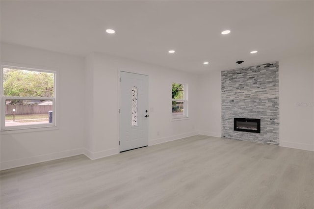 unfurnished living room featuring a stone fireplace, plenty of natural light, recessed lighting, and light wood-style floors