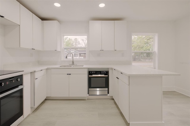 kitchen featuring wall oven, a peninsula, white cabinetry, and a sink