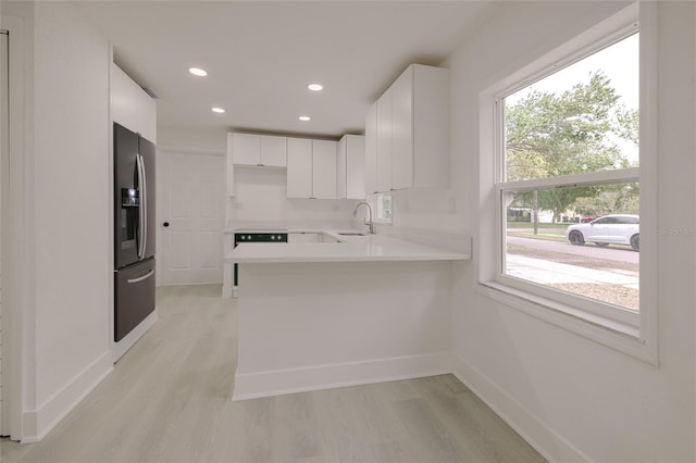 kitchen featuring light wood-type flooring, a sink, refrigerator with ice dispenser, and a peninsula