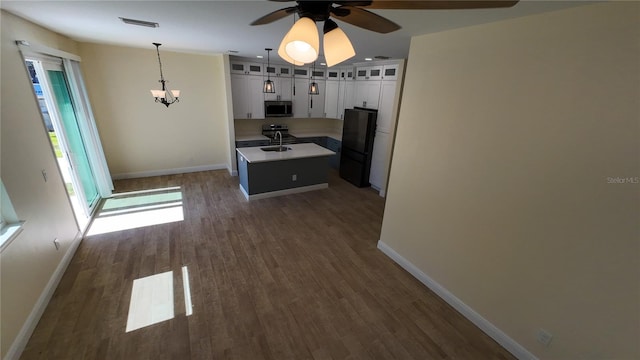 kitchen featuring visible vents, light countertops, freestanding refrigerator, stainless steel microwave, and an island with sink