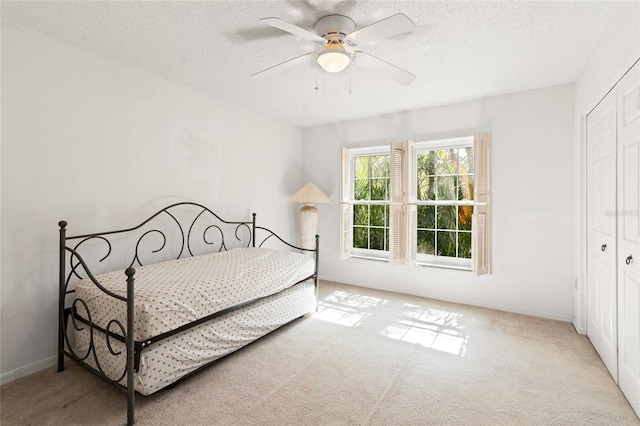 bedroom with a ceiling fan, a closet, light carpet, and a textured ceiling