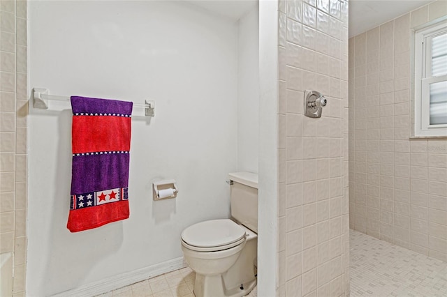 bathroom featuring tiled shower, toilet, and baseboards