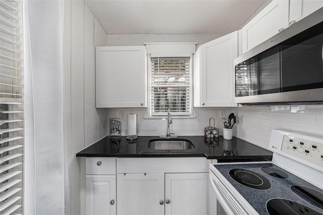 kitchen with white electric stove, stainless steel microwave, decorative backsplash, white cabinets, and a sink