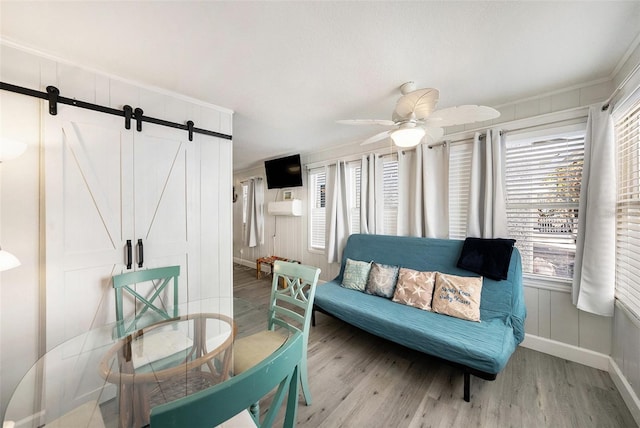 interior space featuring a barn door, wood finished floors, a ceiling fan, and baseboards