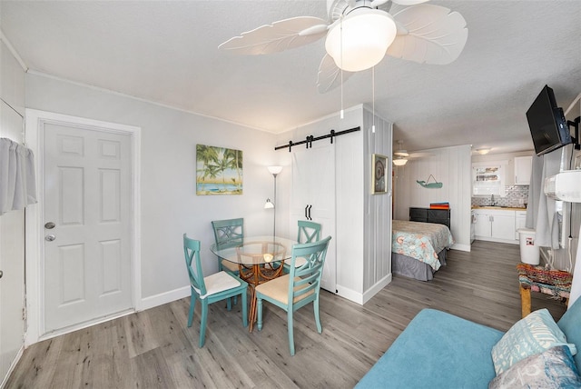 dining area featuring a barn door, baseboards, a ceiling fan, wood finished floors, and a textured ceiling