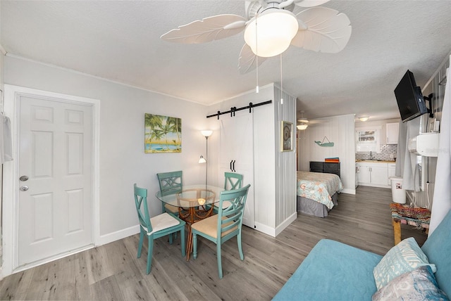 dining area featuring light wood finished floors, a barn door, baseboards, a ceiling fan, and a textured ceiling