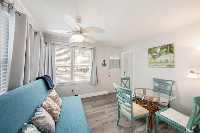 dining space with ceiling fan, a textured ceiling, wood finished floors, baseboards, and crown molding