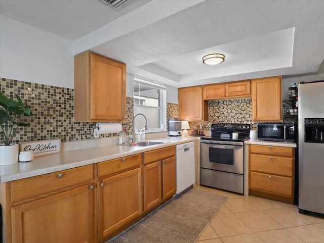 kitchen featuring a raised ceiling, appliances with stainless steel finishes, a sink, light countertops, and backsplash