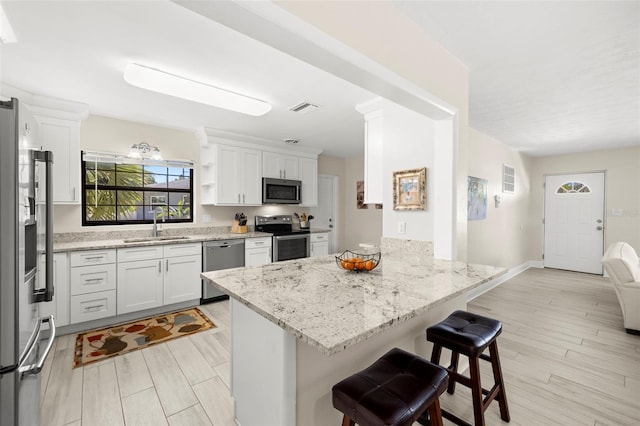 kitchen with a peninsula, a sink, stainless steel appliances, white cabinets, and a kitchen bar