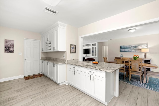 kitchen featuring white cabinetry, a peninsula, light wood finished floors, baseboards, and light stone countertops