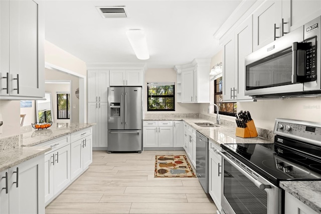 kitchen with visible vents, light stone counters, white cabinets, stainless steel appliances, and a sink