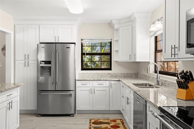 kitchen with light stone countertops, appliances with stainless steel finishes, white cabinetry, and a sink