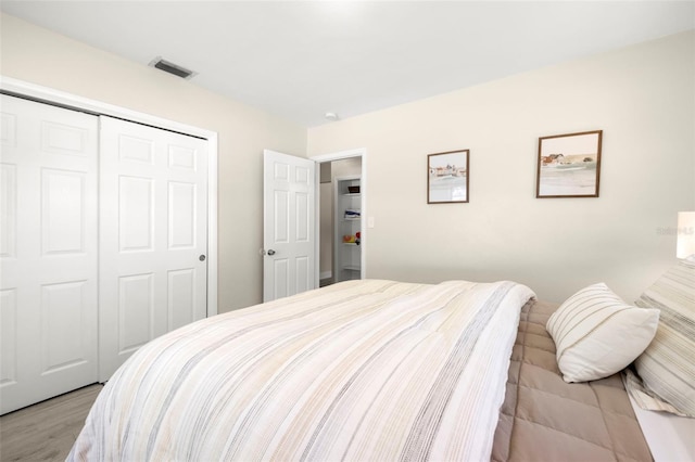 bedroom with visible vents, light wood-style floors, and a closet