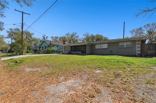 ranch-style house with driveway, stucco siding, fence, and a front yard