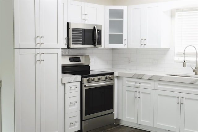 kitchen featuring backsplash, appliances with stainless steel finishes, glass insert cabinets, white cabinetry, and a sink