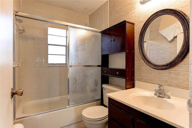 bathroom featuring a textured ceiling, combined bath / shower with glass door, toilet, and vanity