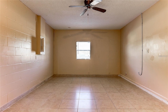 empty room featuring concrete block wall, ceiling fan, a textured ceiling, and light tile patterned floors