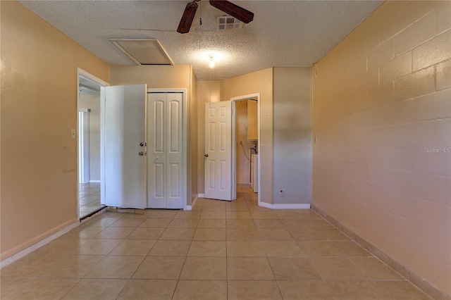 spare room featuring concrete block wall, light tile patterned floors, visible vents, ceiling fan, and a textured ceiling