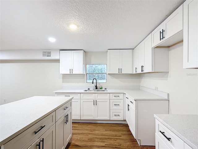 kitchen featuring visible vents, white cabinets, wood finished floors, a textured ceiling, and a sink