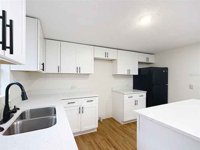 kitchen with freestanding refrigerator, white cabinets, light countertops, and a sink