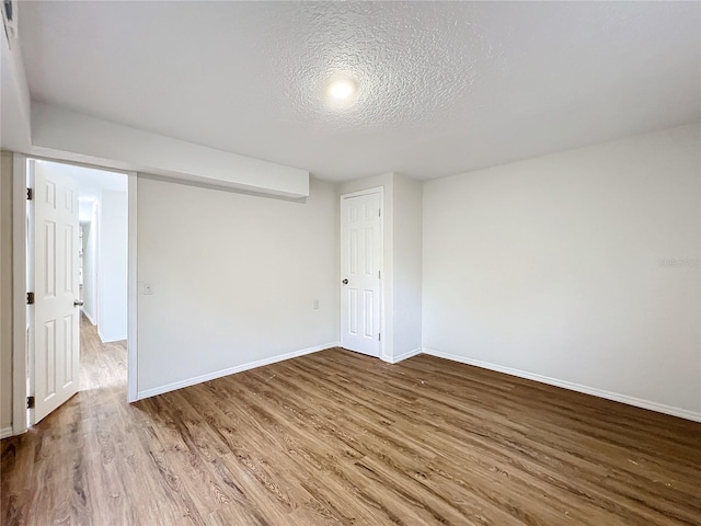 empty room featuring a textured ceiling, baseboards, and wood finished floors