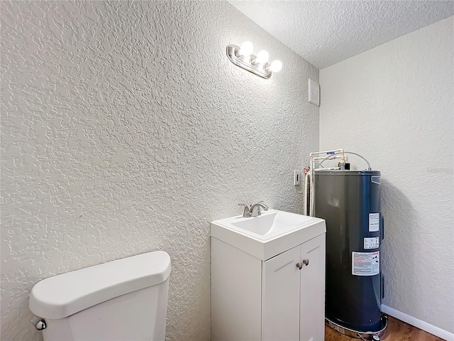 bathroom with visible vents, a textured wall, electric water heater, a textured ceiling, and vanity