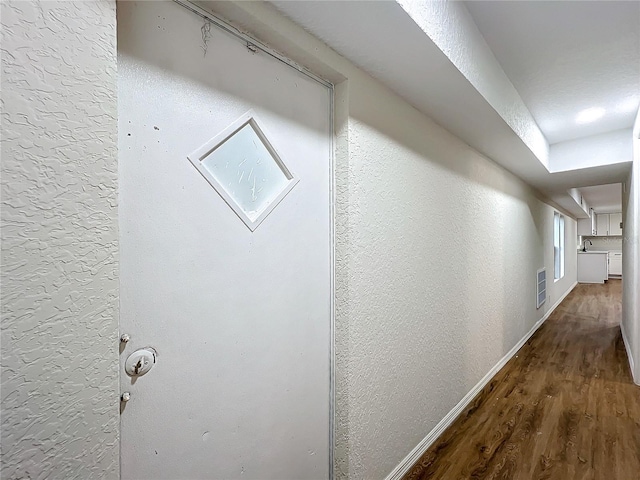 hall with visible vents, a textured wall, baseboards, and wood finished floors