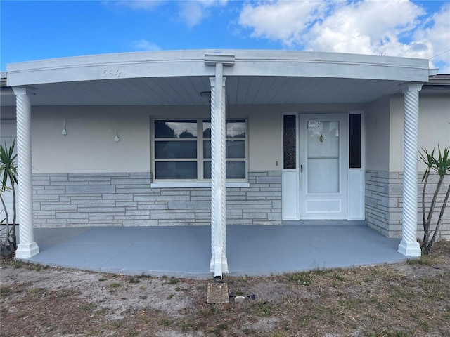 entrance to property with stone siding, a porch, and stucco siding