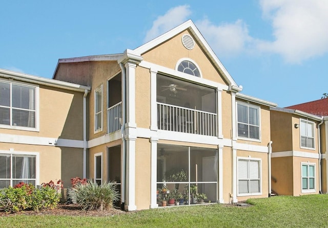 back of property with a ceiling fan, a yard, and stucco siding