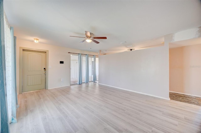 empty room featuring light wood finished floors, a barn door, baseboards, and ceiling fan