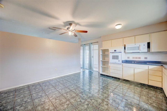 kitchen featuring dark countertops, decorative backsplash, a ceiling fan, white appliances, and baseboards