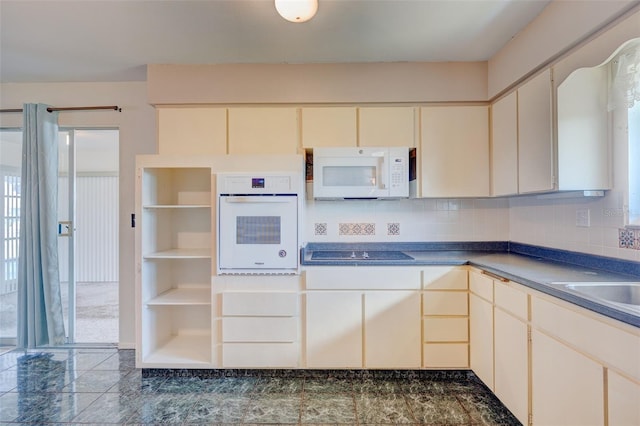 kitchen with white appliances, dark countertops, cream cabinetry, and tasteful backsplash