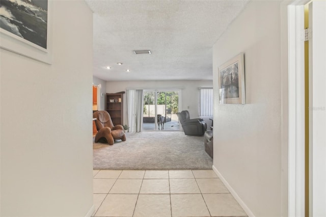 hallway with visible vents, light colored carpet, light tile patterned flooring, a textured ceiling, and baseboards