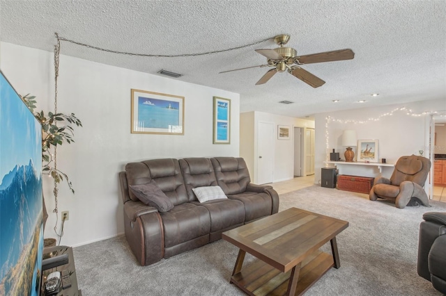 living room featuring a ceiling fan, visible vents, a textured ceiling, and light colored carpet