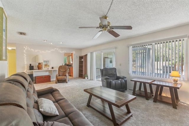 living area with a ceiling fan, light colored carpet, visible vents, and a textured ceiling